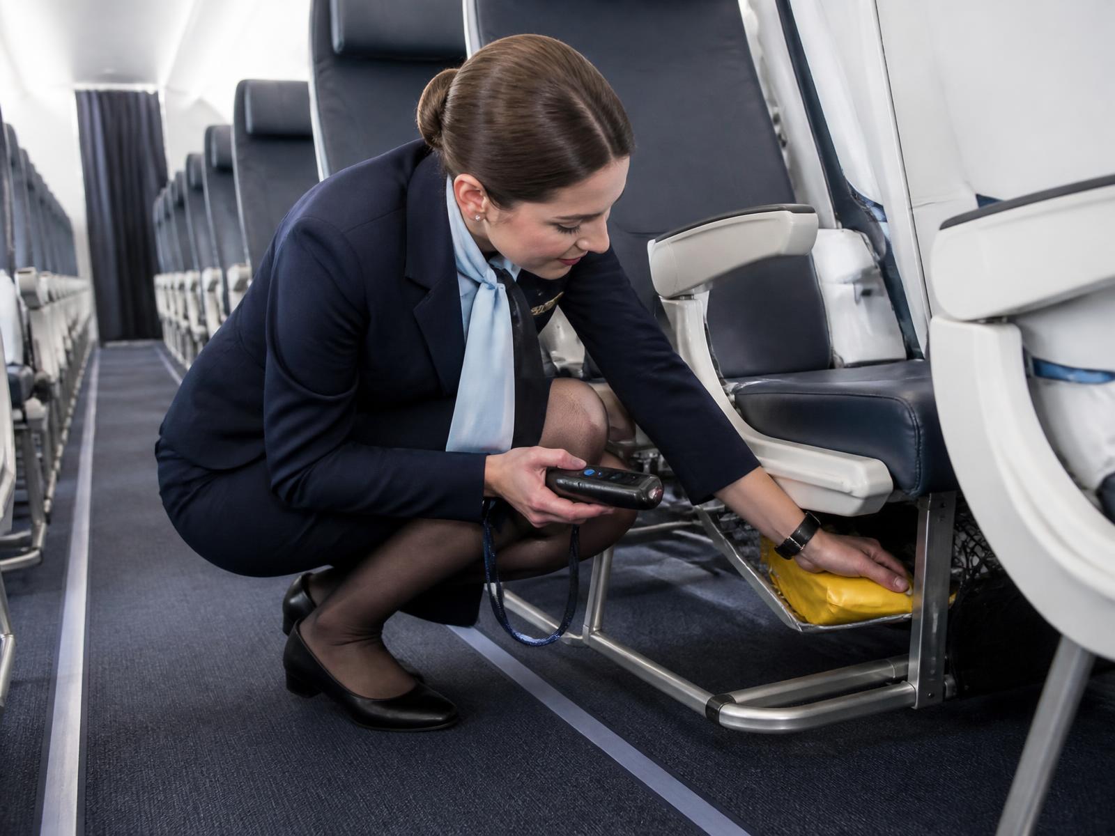 Cabin crew member scanning safety equipment under a passenger seat