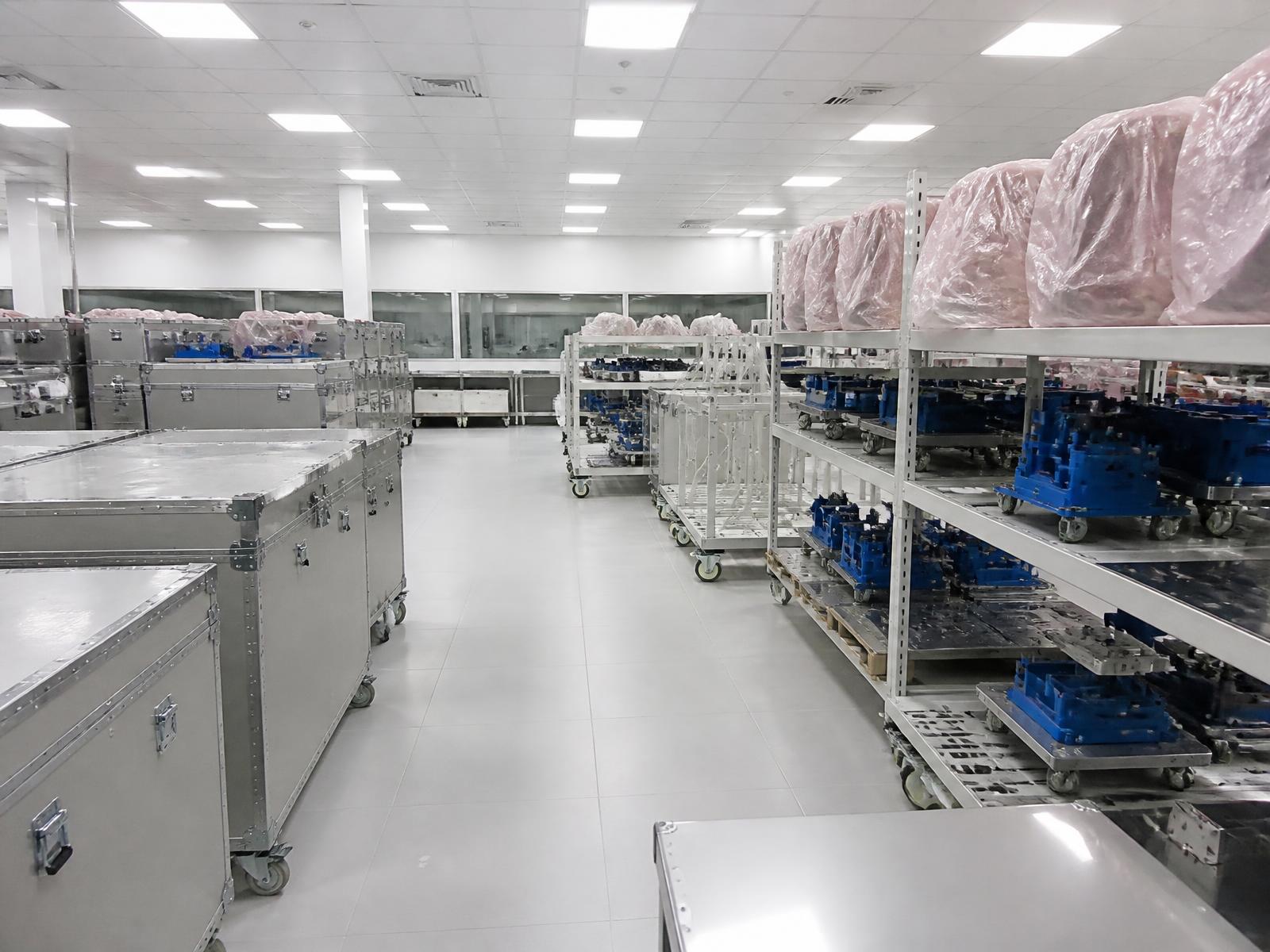 Anodised transport containers and ground support equipment on racks under protective covers in a bright cleanroom storage area